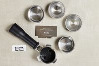 Closeup of various Breville Bambino Plus Espresso Machine filter parts on cream surface