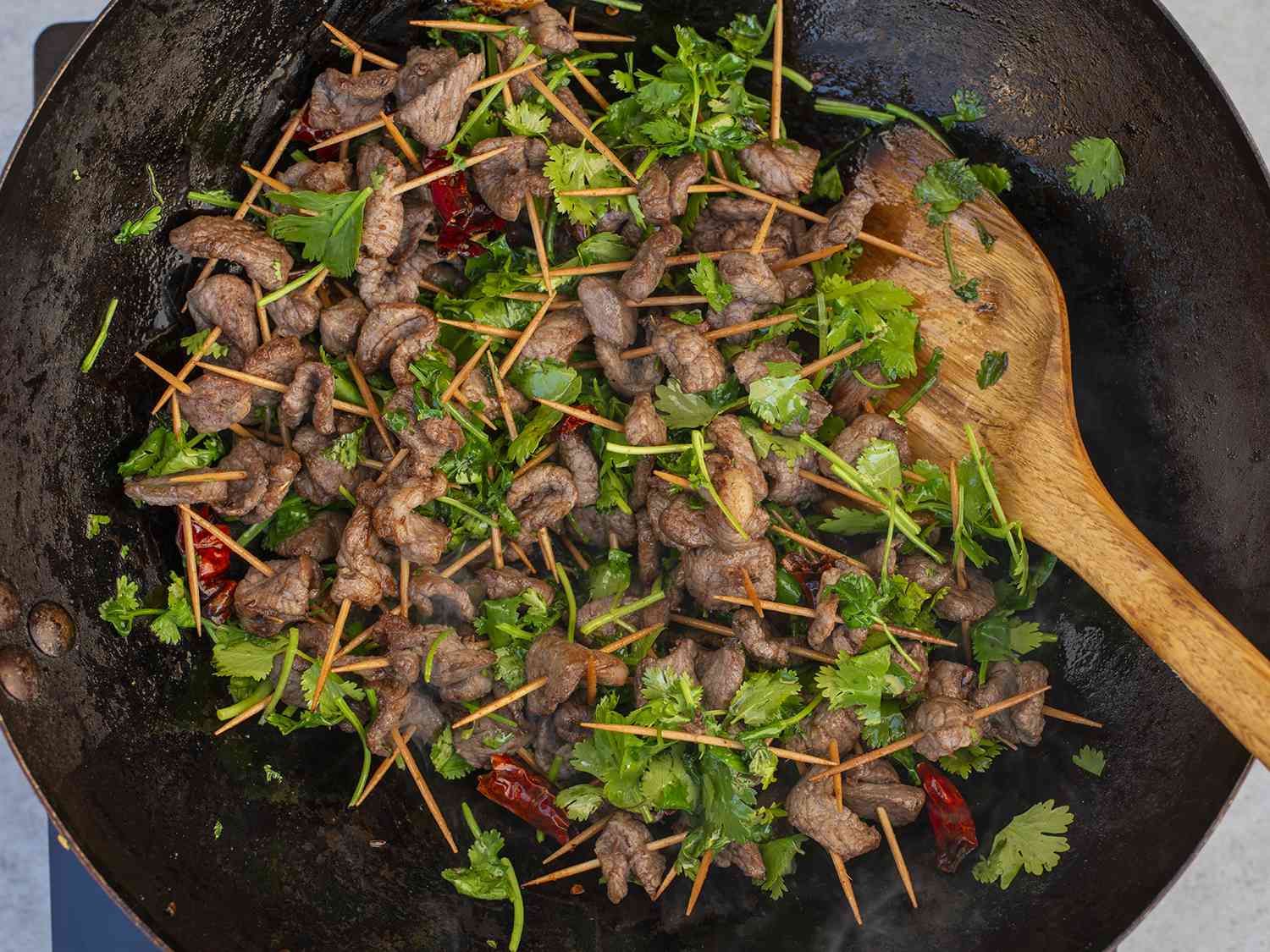 Lamb toothpicks tossed in a wok with aromatics