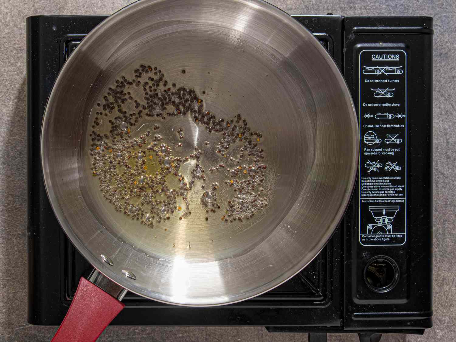 Pan on a lit stovetop with seeds roasting in oil preparation for a cooking recipe step