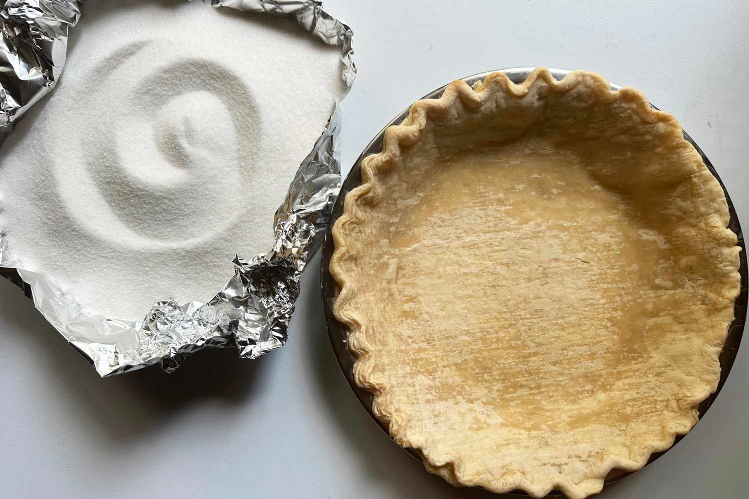 A par-baked pie shell next to a foil liner full of granulated sugar.