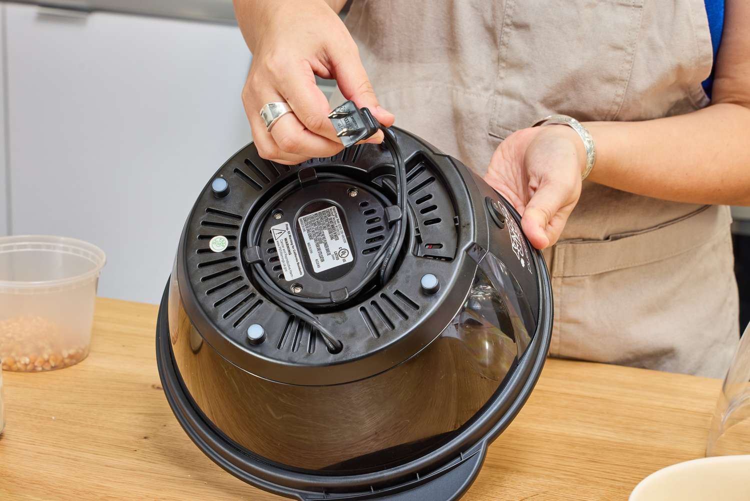 A person winds the power cord around the base of the West Bend Stir Crazy Electric Hot Oil Popcorn Popper