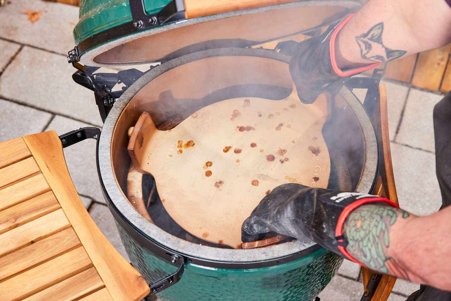 A person places a pizza stone inside the Big Green Egg Large Charcoal Kamado Grill and Smoker