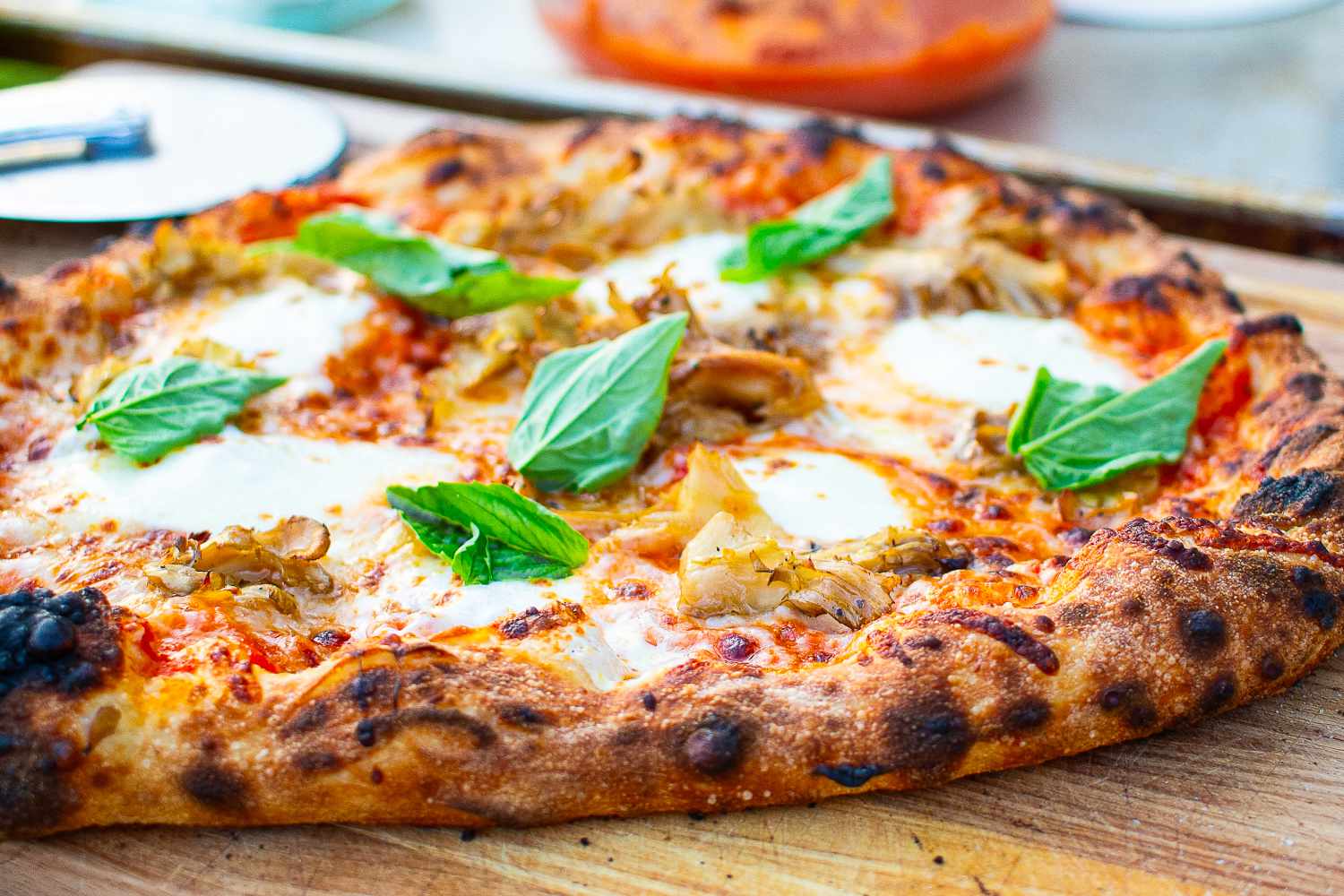 Pizza with basil leaves, cheese, and roasted toppings on a wooden board after leaving the Solo Stove Pi Prime