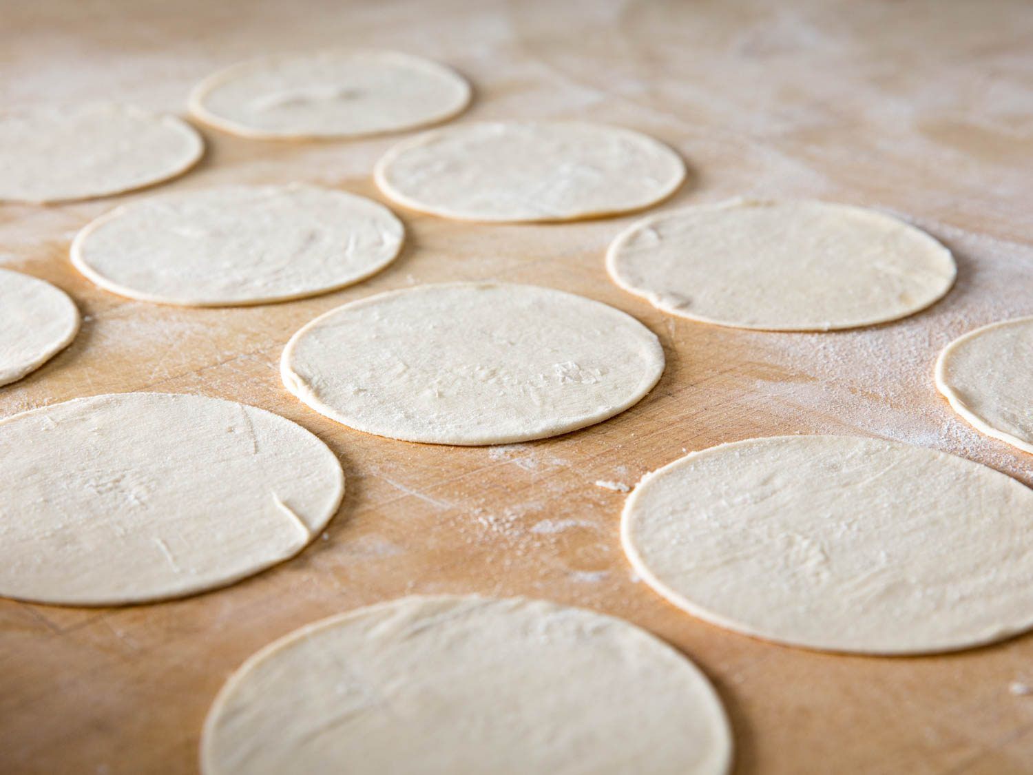 12 rounds of cannoli dough laying on a floured surface, ready to be formed and fried.