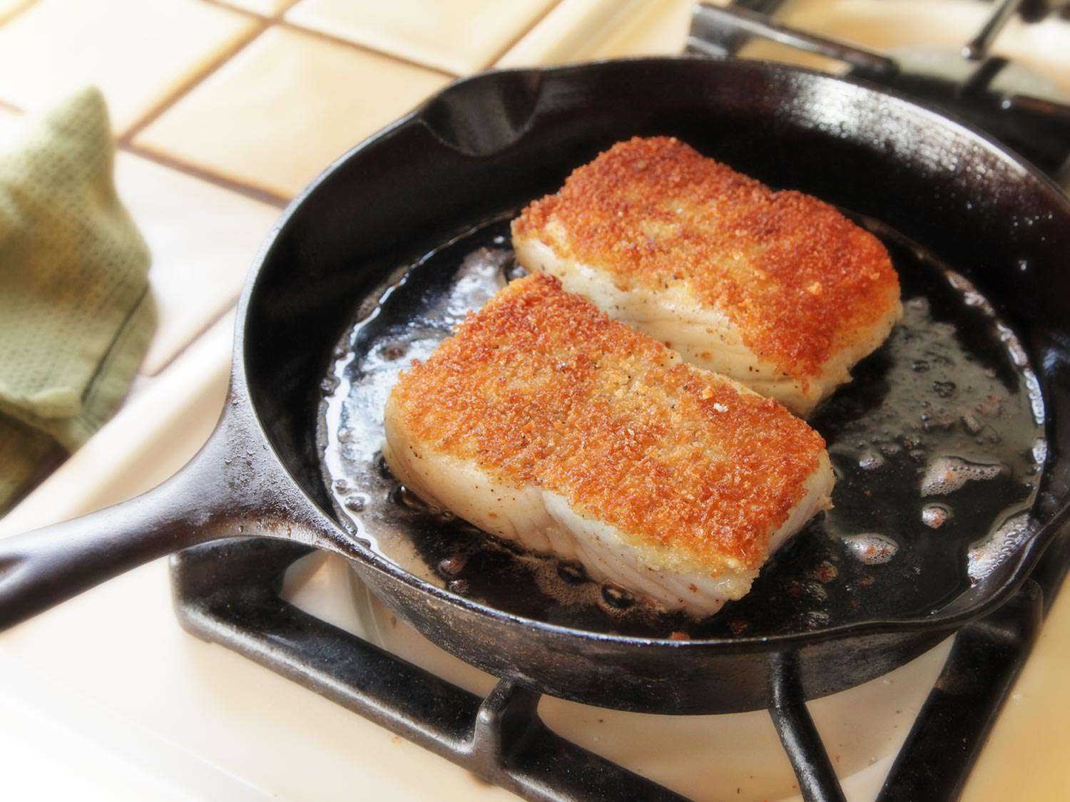 The fillet portions, frying in the cast iron skillet with their breadcrumb side facing up.