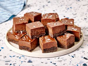 A plate of layered chocolate squares with a fudgy and textured appearance topped with sea salt