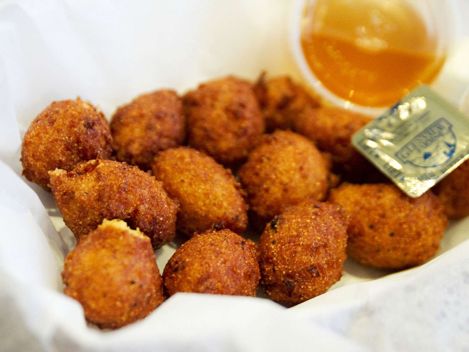 Hushpuppies in a parchment lined basket with melted butter off to the side.