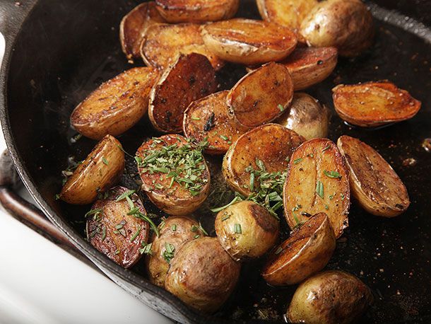 Crispy browned fingerling potato halves in skillet tossed in basting butter and herbs.