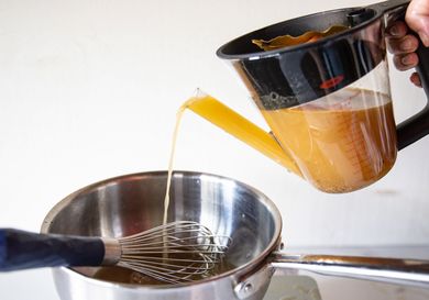 Pouring broth from a container into a saucepan with a whisk inside