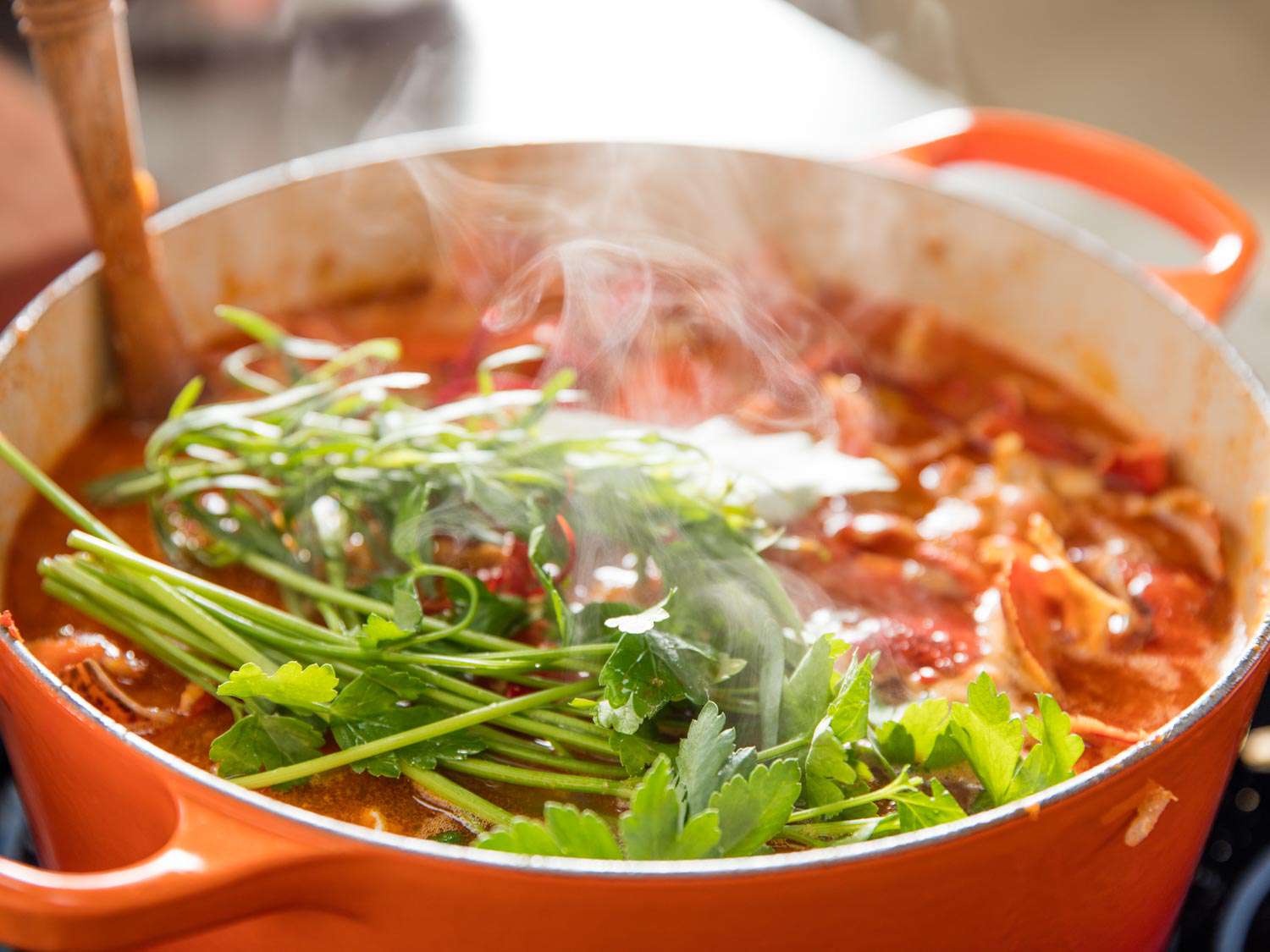 Sprigs of parsley and tarragon piled on the the surface of the lobster stock, about to be stirred in.