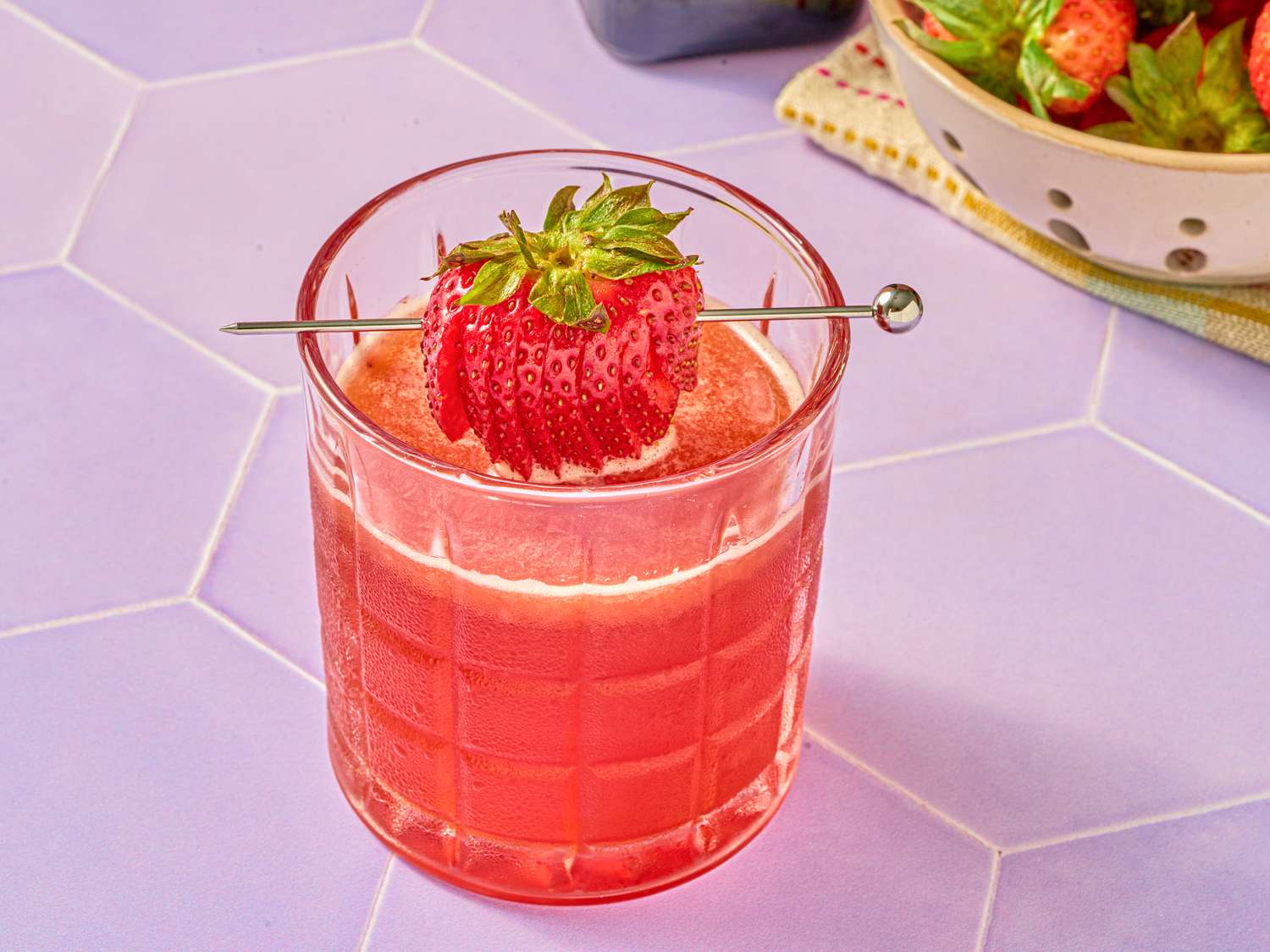 A glass of strawberry smash cocktail with a whole strawberry garnish