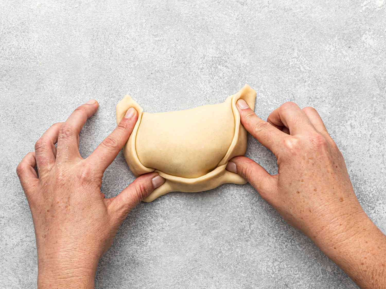 Hands folding dough to form a Chilean beef empanada.