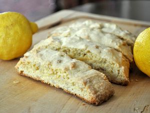 Closeup of lemon pine nut biscotti on a cutting board, flanked by two lemons.