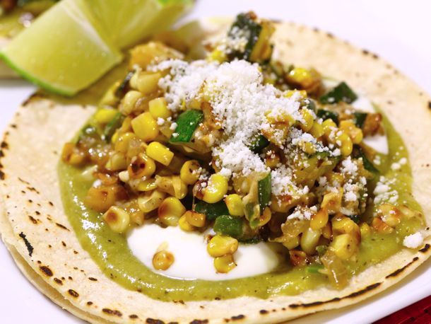Cotija cheese on a taco with corn and lime wedges.