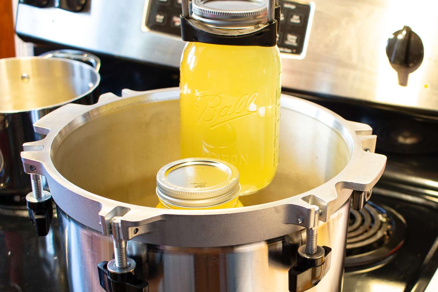 Canning tongs removing jars of chicken stock from a pressure canner.