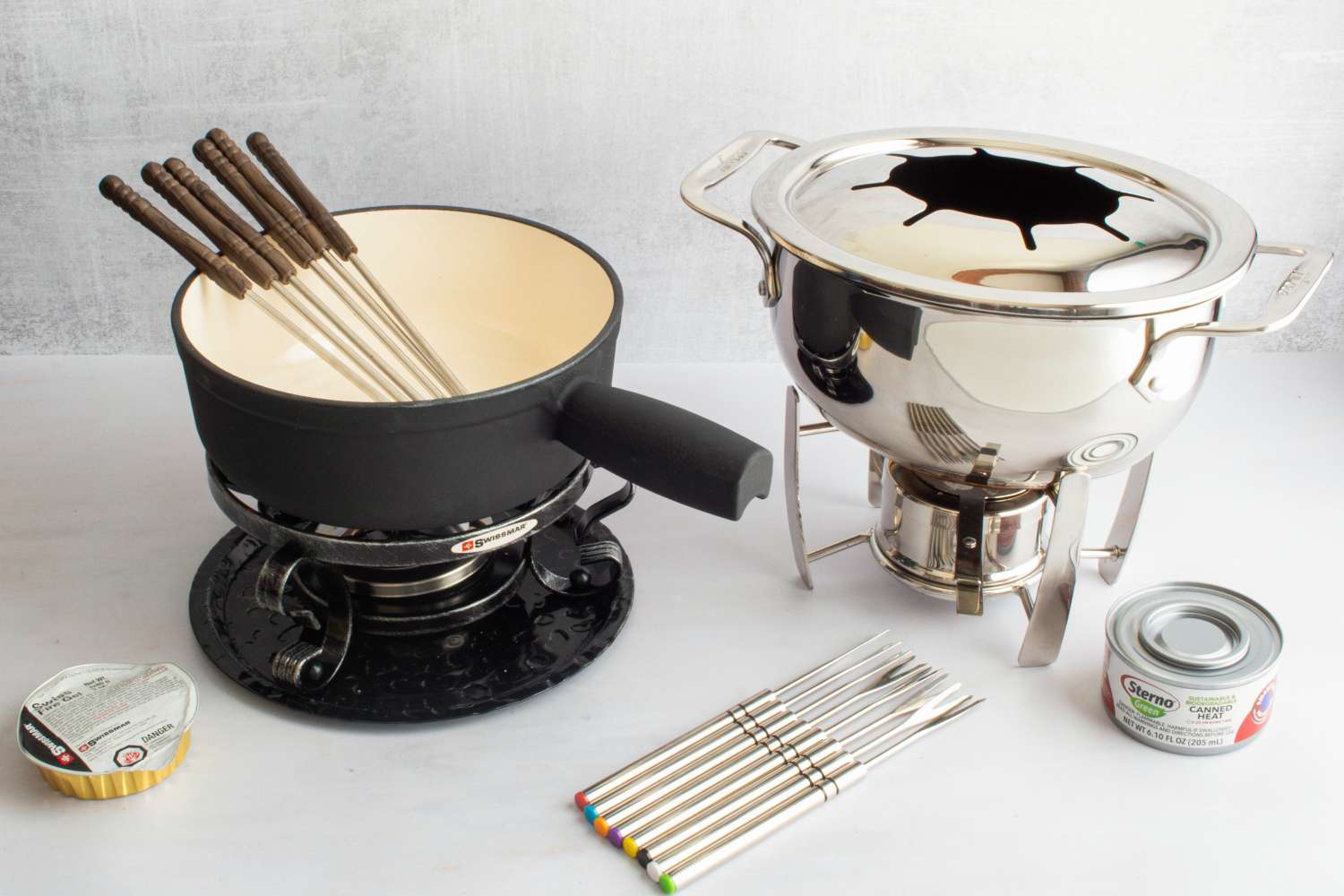 Two traditional fondue pots beside cans of fuel and fondue forks.