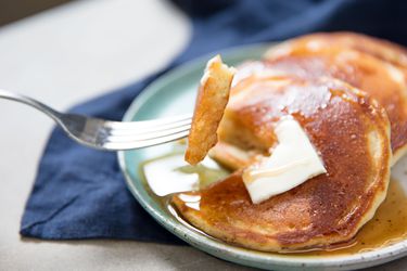 A fork piercing a double-layer portion of golden light and thin fluffy pancakes drenched in maple syrup and butter