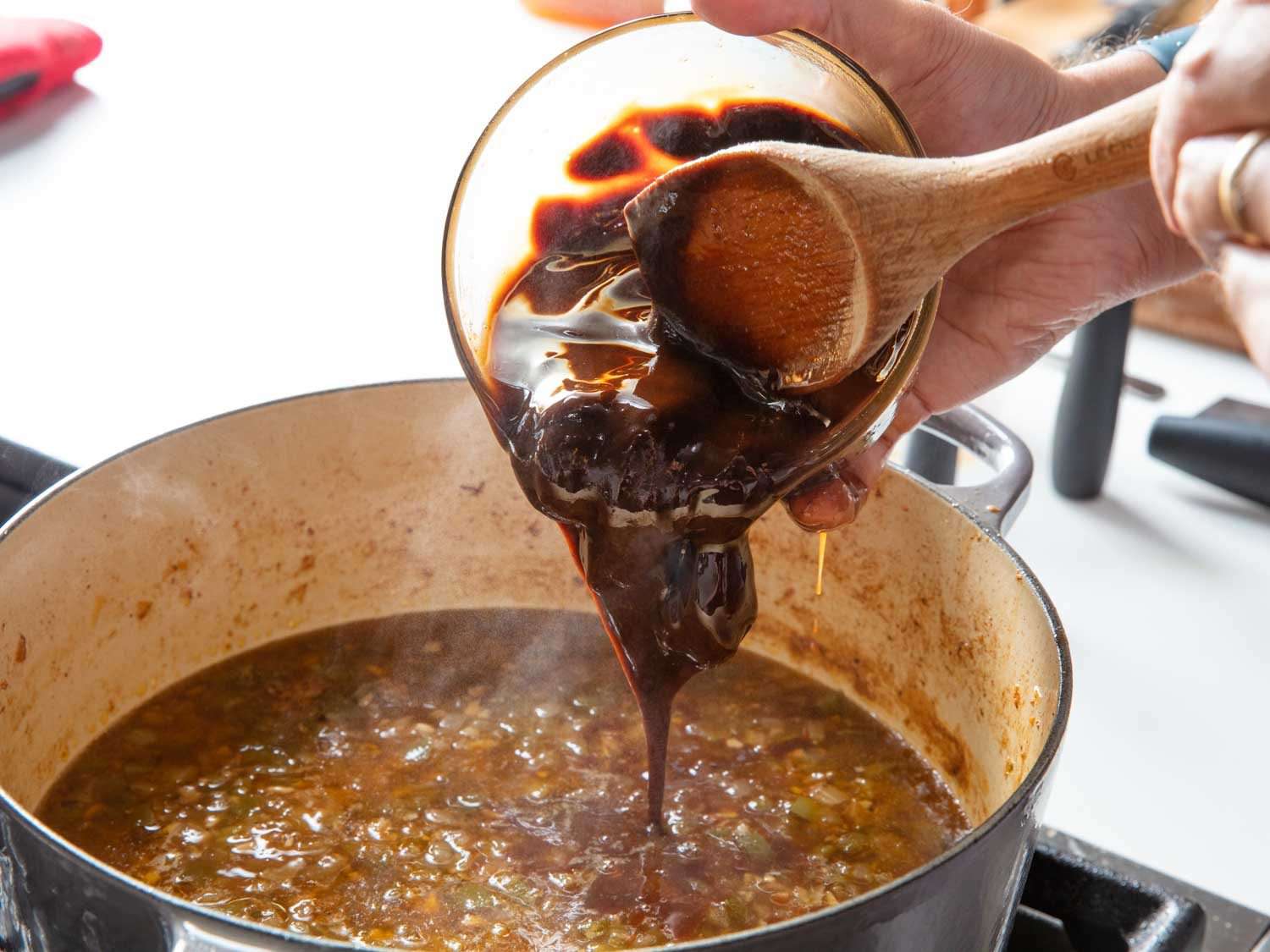 Adding a roux to the pot of gumbo with a wooden spoon.