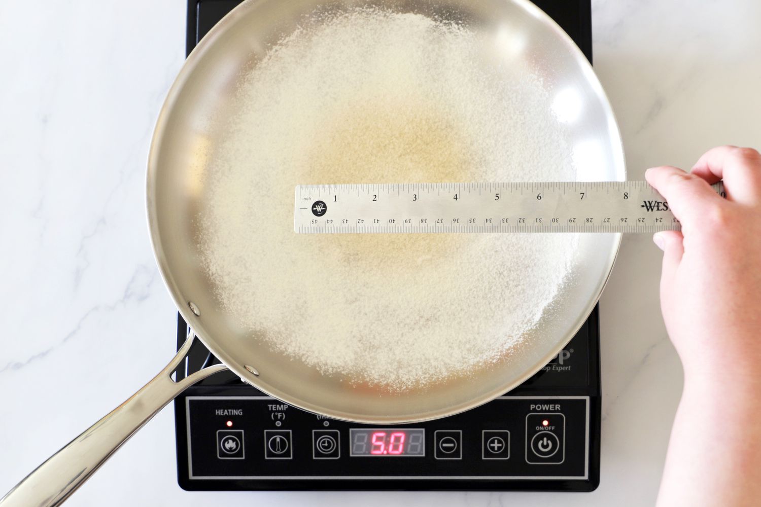 A person measuring a toasted flour hot spot in a pan on an induction burner