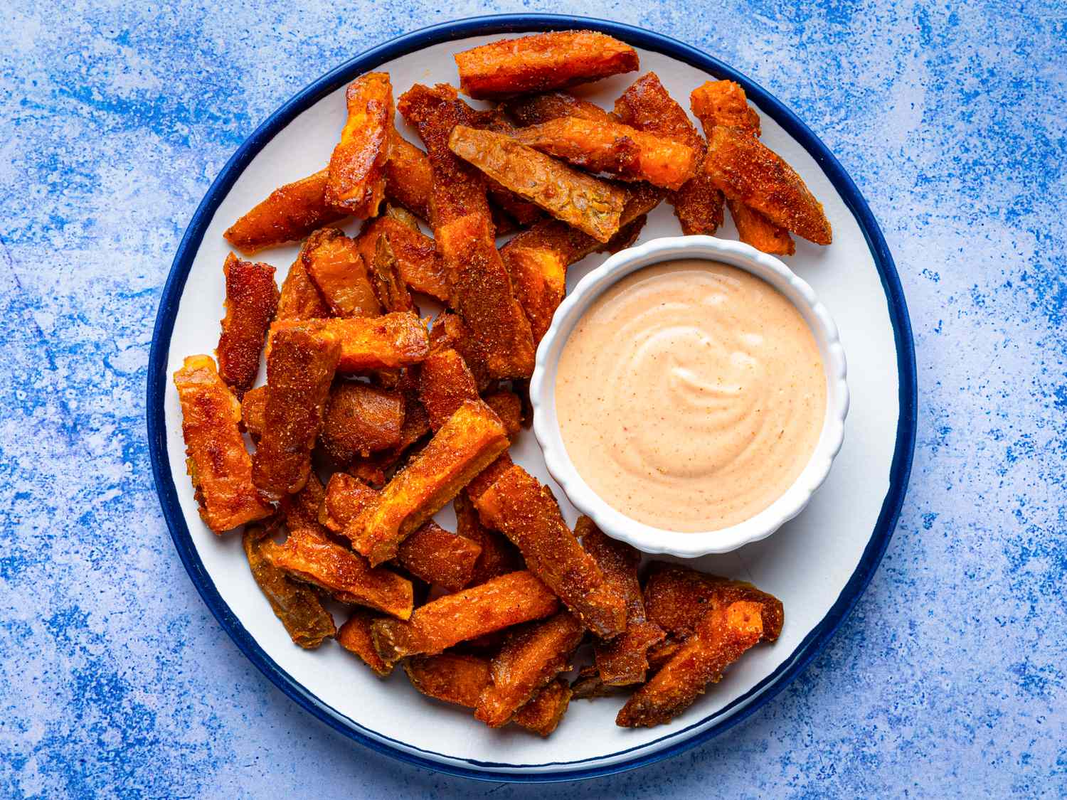 A plate of sweet potato fries served with a dipping sauce in a small dish
