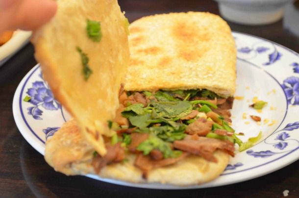A beef sandwhich, or niu rou shao bing. The author holds up the top half of the wheat cake to reveal the beef filling inside.