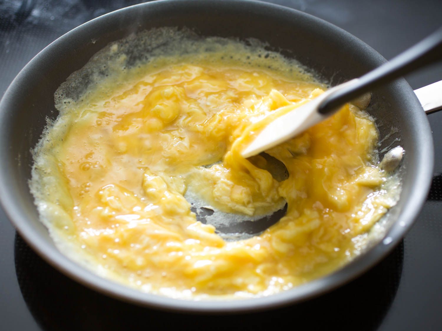 Stirring scrambled eggs with a silicon spatula in a non-stick pan.