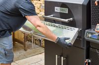 A person extends the shelf on the Masterbuilt Gravity Series 1150 Digital Charcoal Grill and Smoker