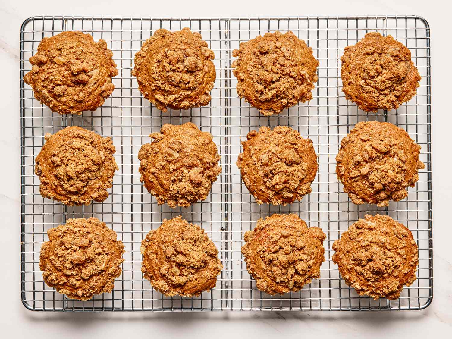 Twelve spiced gingerbread muffins topped with crumble cooling on a wire rack