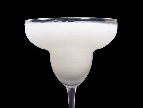 Closeup of frozen lime margarita served up in classic stemmed margarita glass against black background