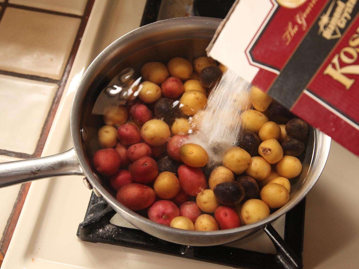 Pouring kosher salt out the of box into pot of small new potatoes in water