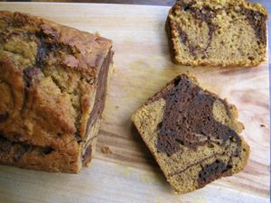Overhead view of a loaf of marbled chocolate pumpkin bread being cut into slices.