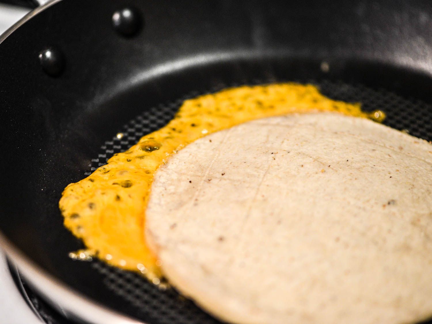 A tortilla on top of melted cheddar on a nonstick pan