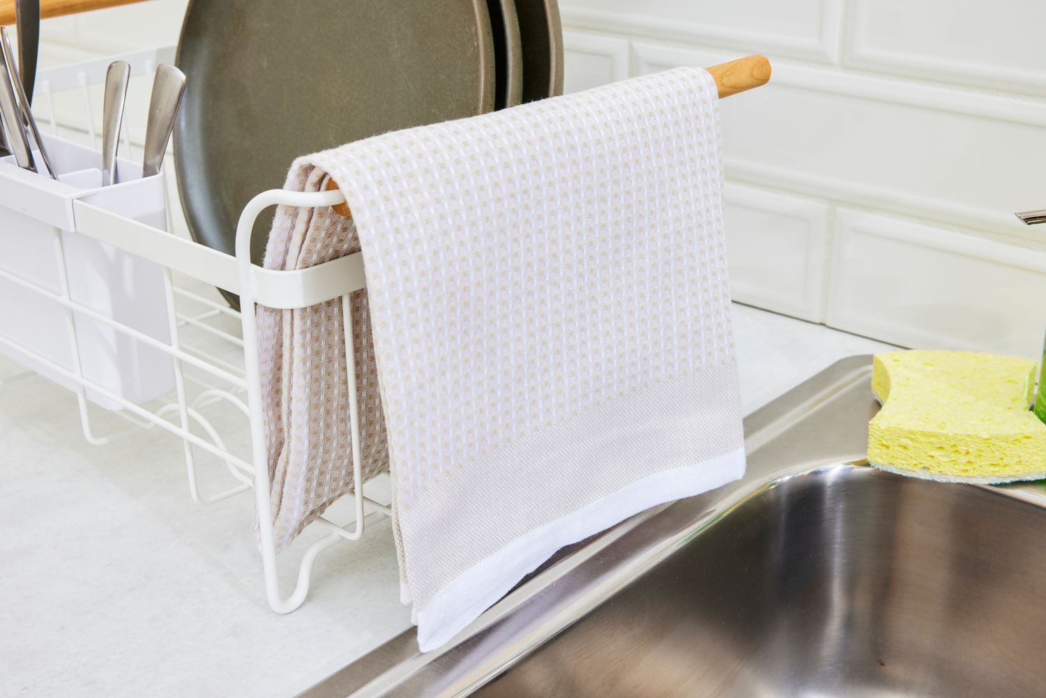 A tan kitchen towel hanging off of a dish rack.