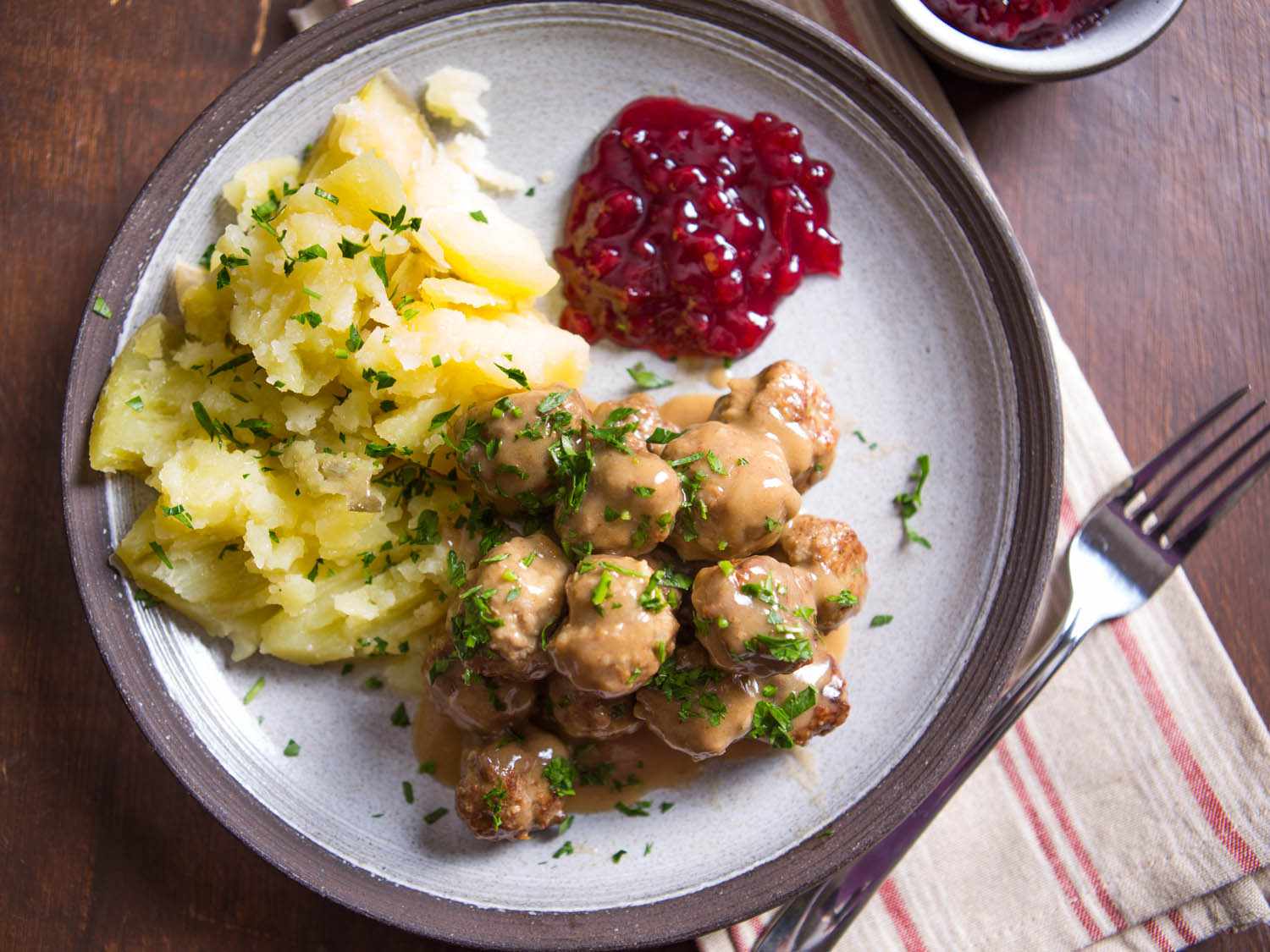 A plate of gravy-covered Swedish meatballs, mashed potatoes, and lingonberry jam. 
