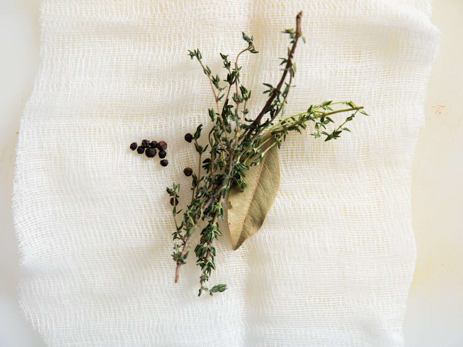 Aromatic herbs and peppercorns on a square of cheesecloth.