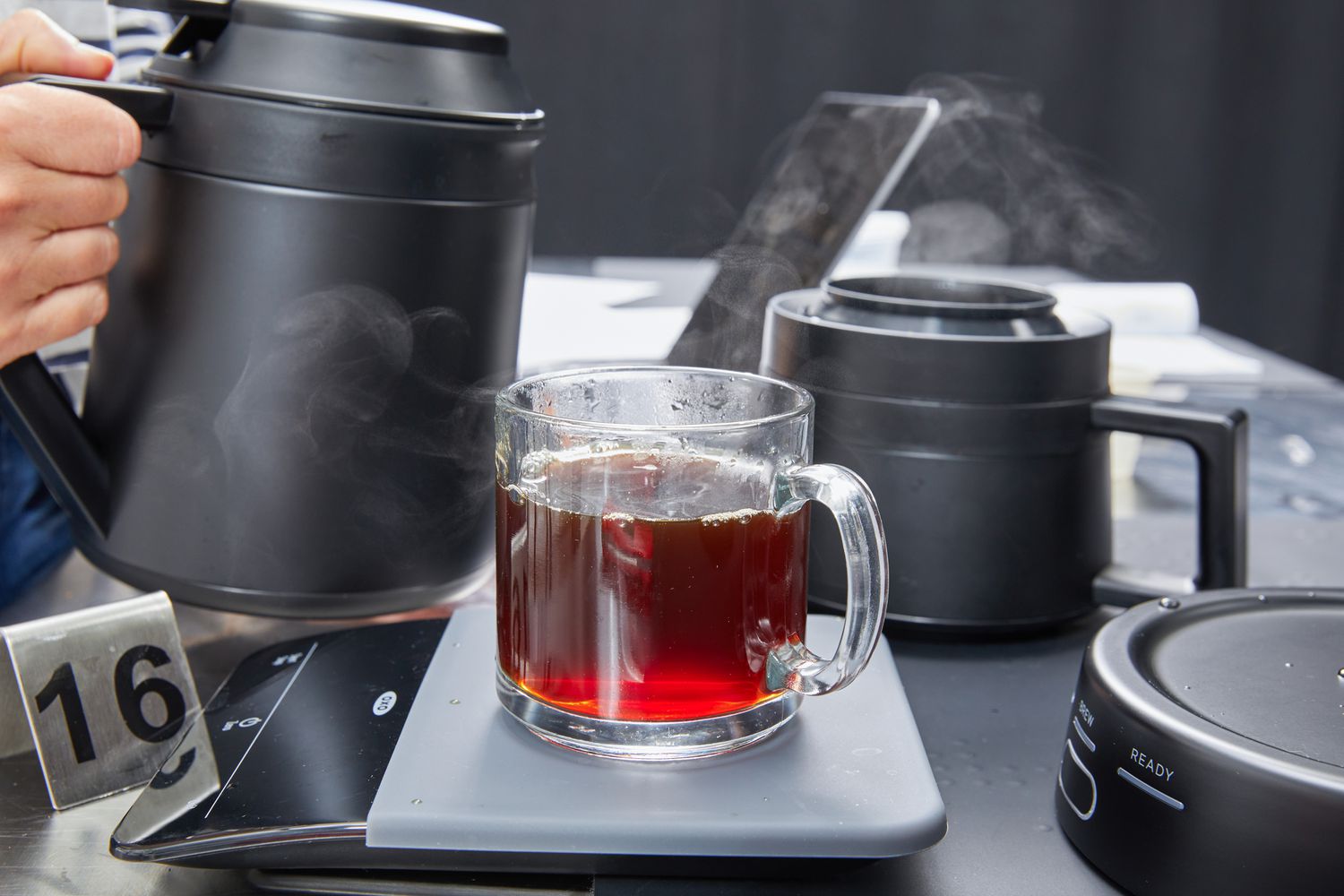 Coffee in a mug on a scale next to a hand holding the Ratio Six Coffee Maker's carafe.