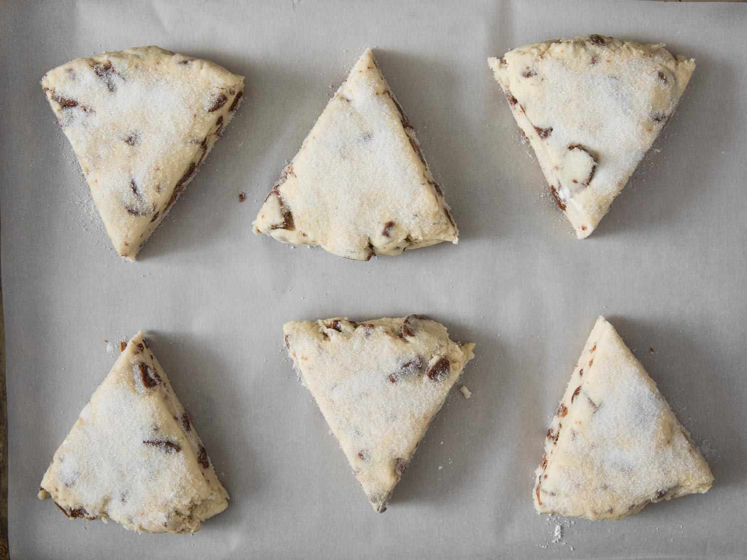 Overhead shot of wedges of unbaked chocolate chip scones on parchment-covered baking sheet.