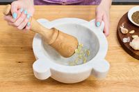 A person using a marble mortar and pestle to crush garlic.