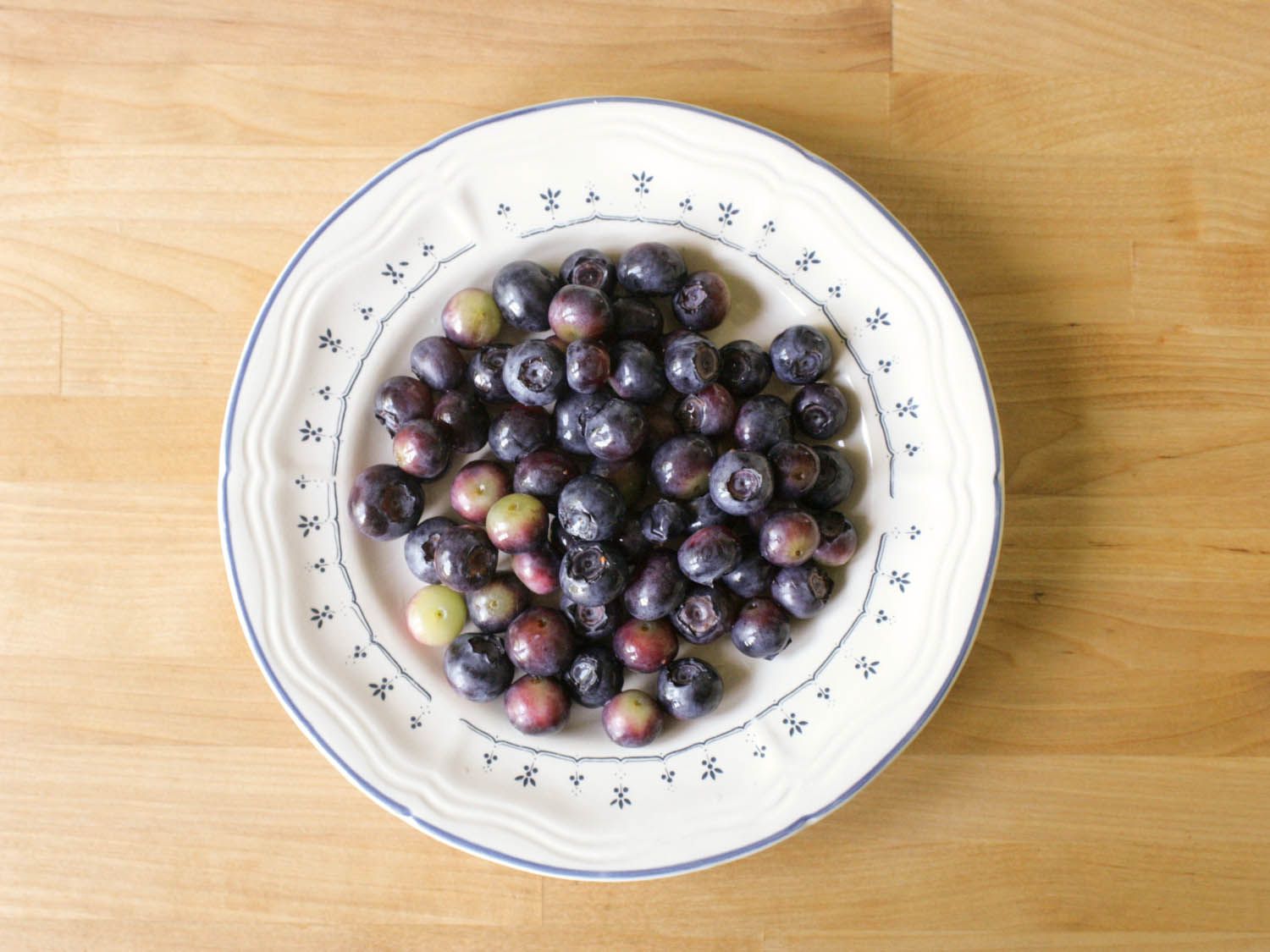 A porcelain plate holding a mix of ripe and unripe blueberries.