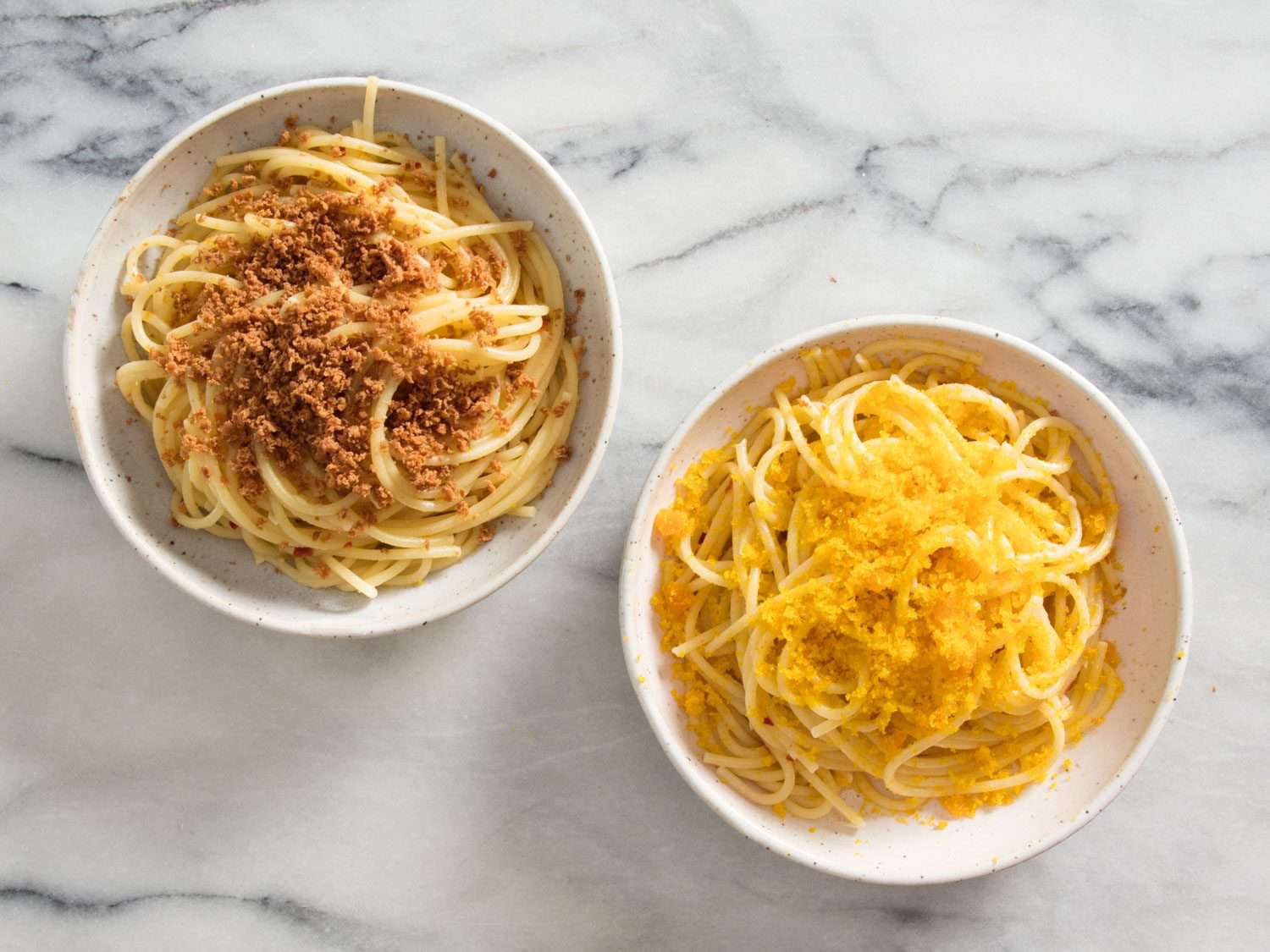 Two bowls of pasta side by side, with tuna bottarga grated over bowl on left, and mullet bottarga grated over bowl on right.