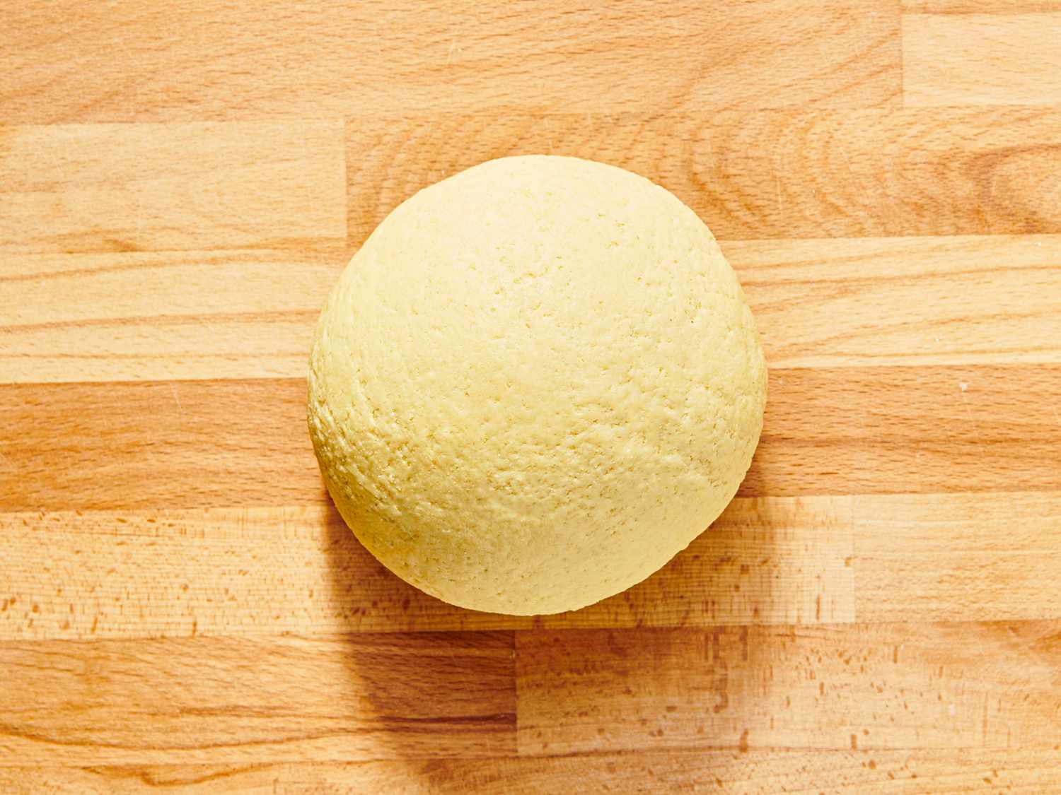 Dough fully formed into a ball on wooden surface 