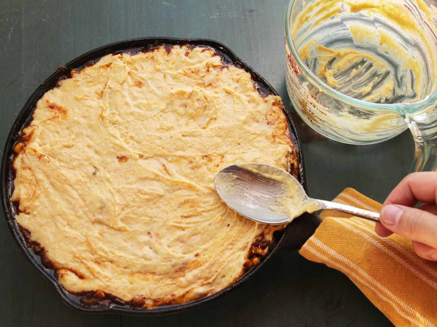 Smoothing cornbread batter on top of tamale pie in cast iron skillet