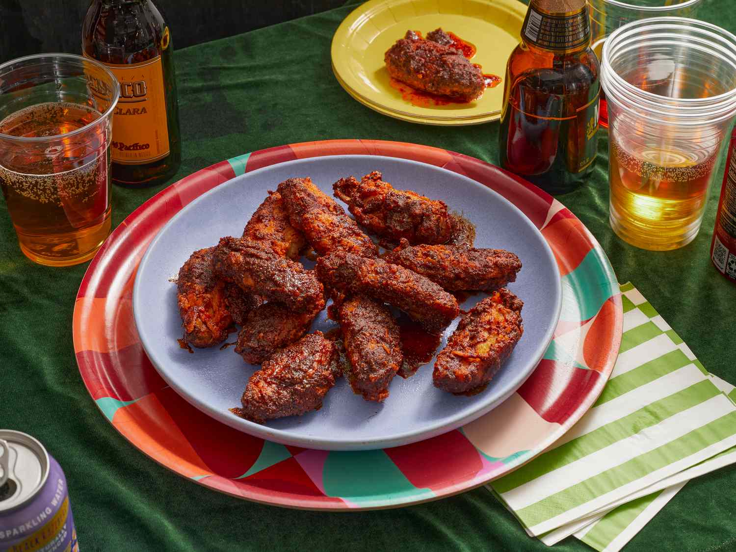 Wings on game day. Blue plate of spicy chicken wings on a colorful platter, beers and green tabletop