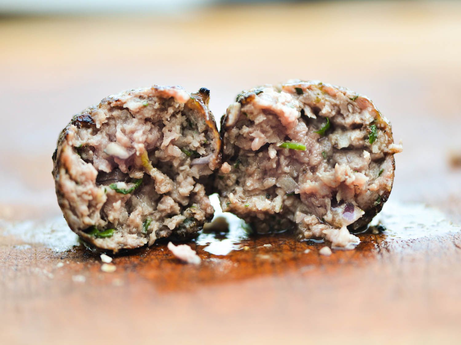 Cross-section of a grilled sheftalia that's been cut in half. The interior looks moist and juices have pooled on the cutting board below.
