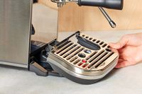Person's hand adjusting tray of Breville Bambino Plus Espresso Machine on a cream counter