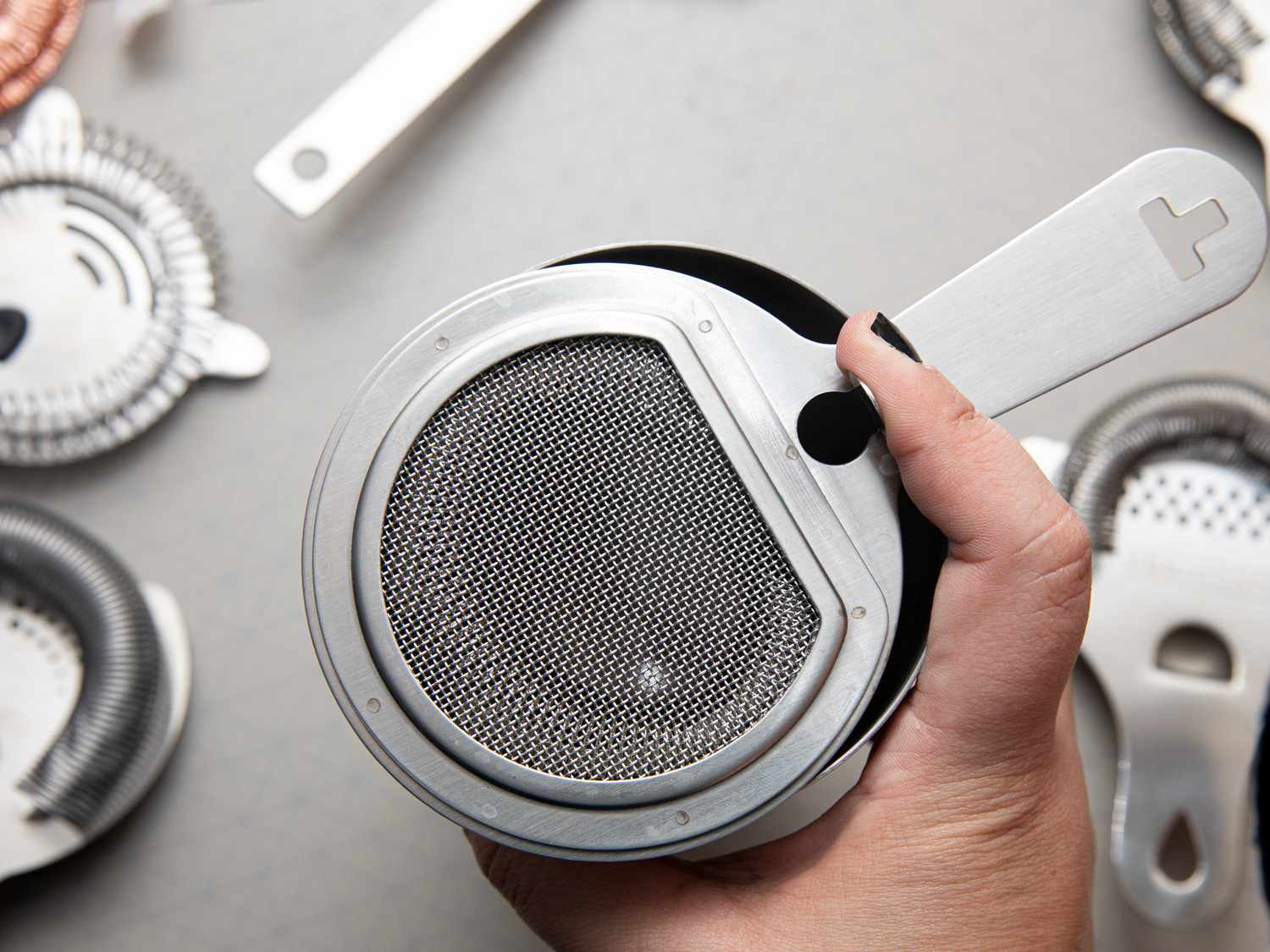 A hand closing the gate on a hawthorne strainer set in a cocktail tin