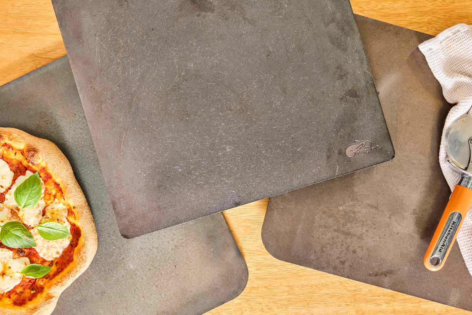 Three pizza steels on a wooden countertop.