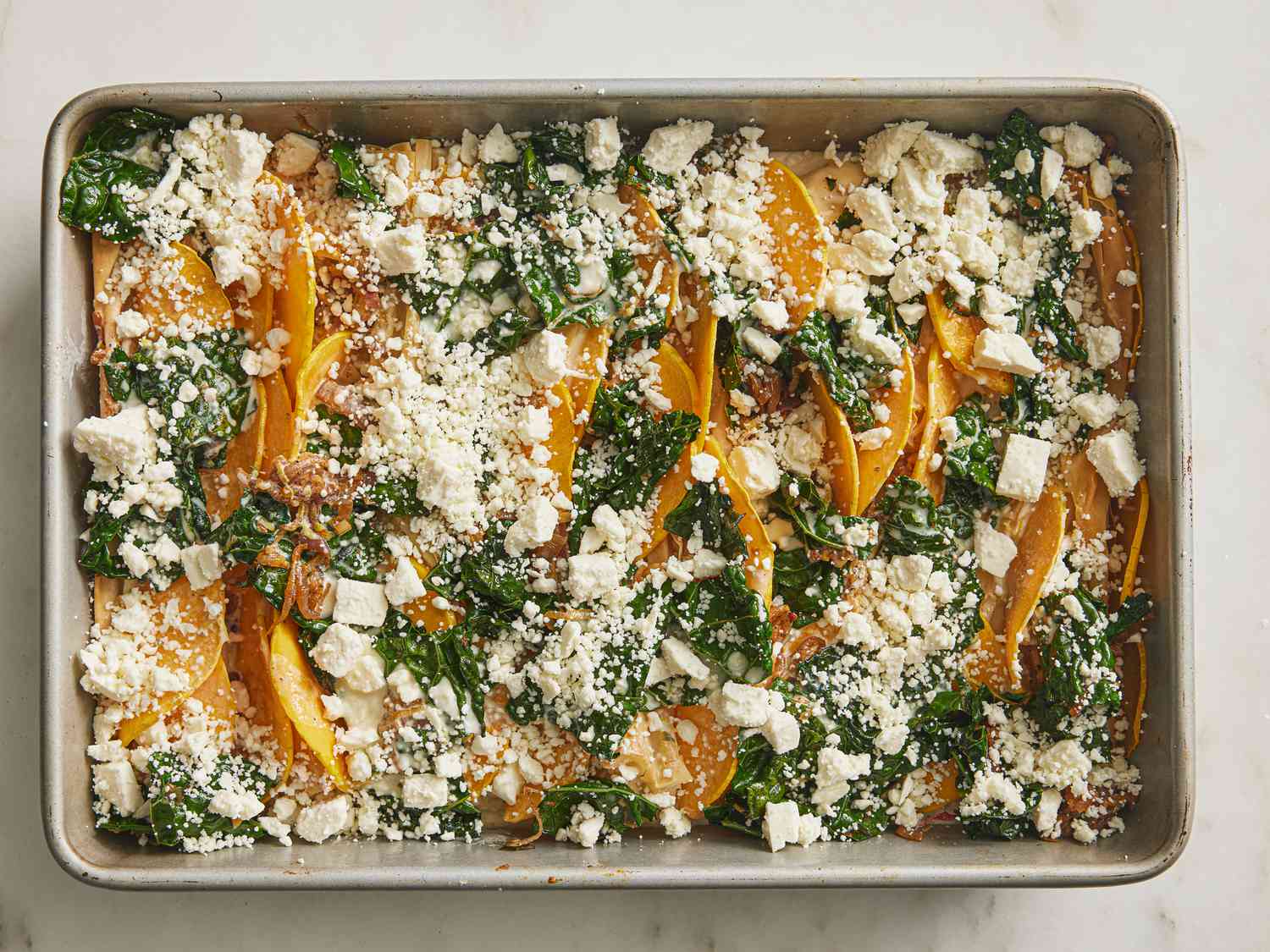 Feta cheese layer on top of vegetables and phyllo dough in a baking sheet 