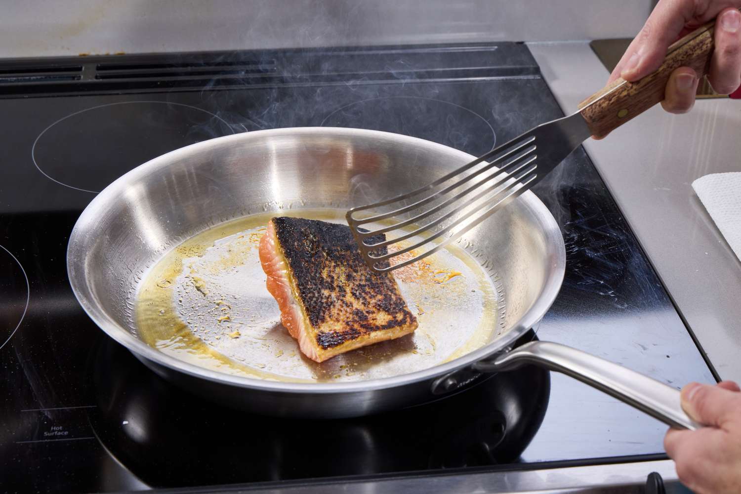 A person cooks a piece of salmon in the Made In 12-Inch Stainless Steel Skillet