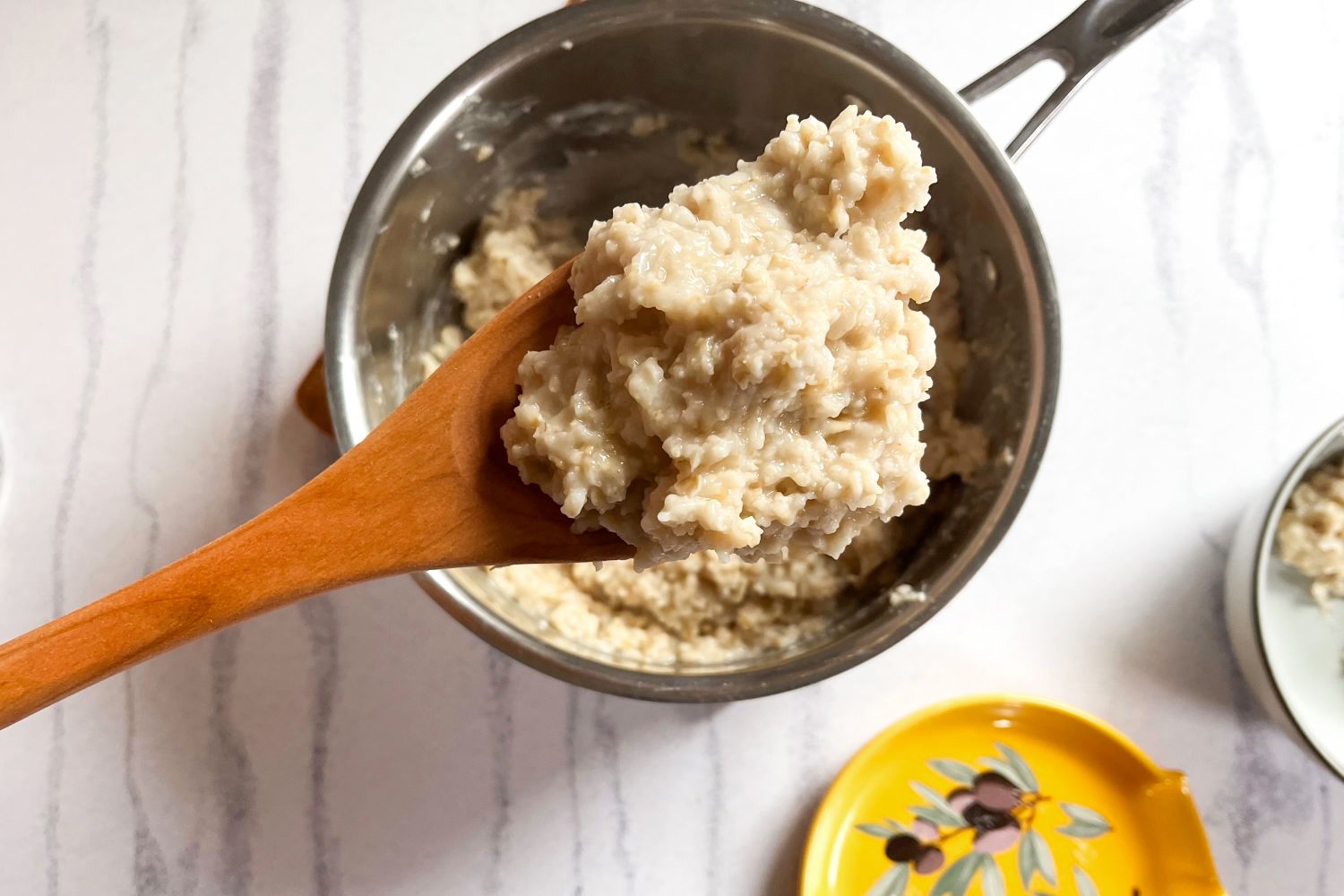 Cooked oatmeal in a FAAY Teak Cooking Spoon held over a pot